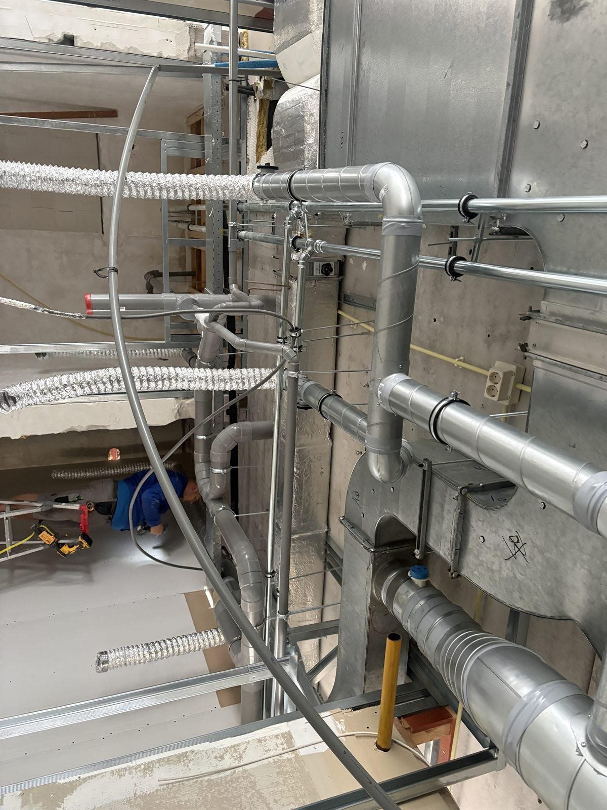 Kanaalwerk en leidingen boven het plafond in een bedrijfspand in aanbouw, monteur aan het werk